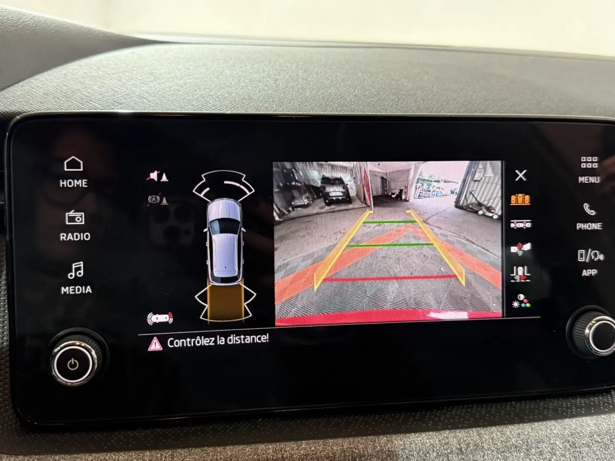 Écran tactile central du Skoda Kamiq rouge 2024 montrant la caméra de recul avec aides au stationnement.
