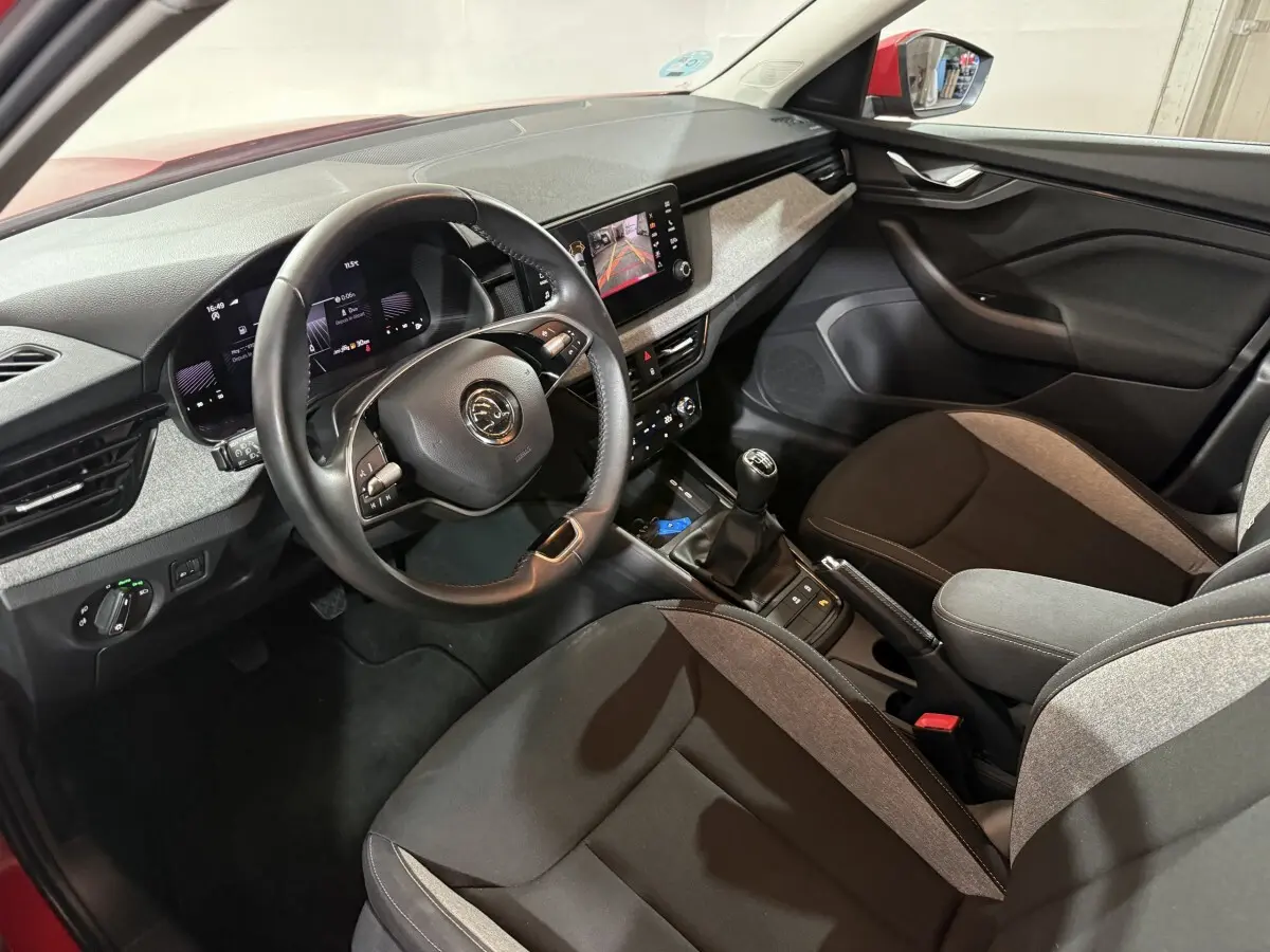 Vue intérieure côté conducteur du Skoda Kamiq 2024 rouge, volant cuir multifonctions et écran tactile central visible.