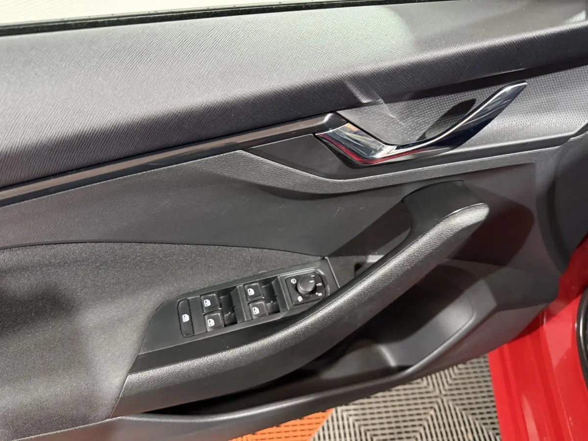 Détail de la porte côté conducteur d’une Skoda Kamiq rouge, montrant les commandes des vitres et rétroviseurs.