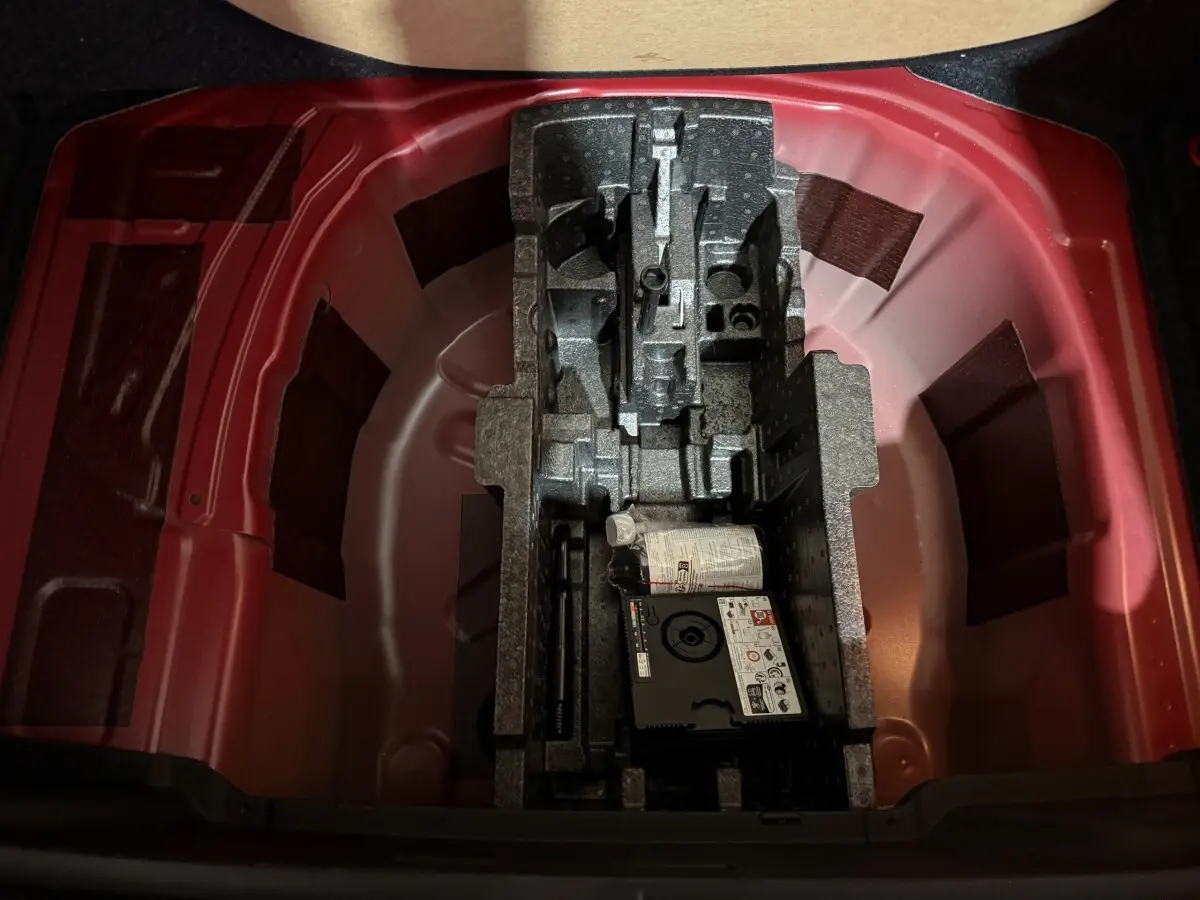 Vue plongeante sur le coffre rouge du Skoda Kamiq 2024, montrant le rangement sous plancher avec kit de réparation pneus.