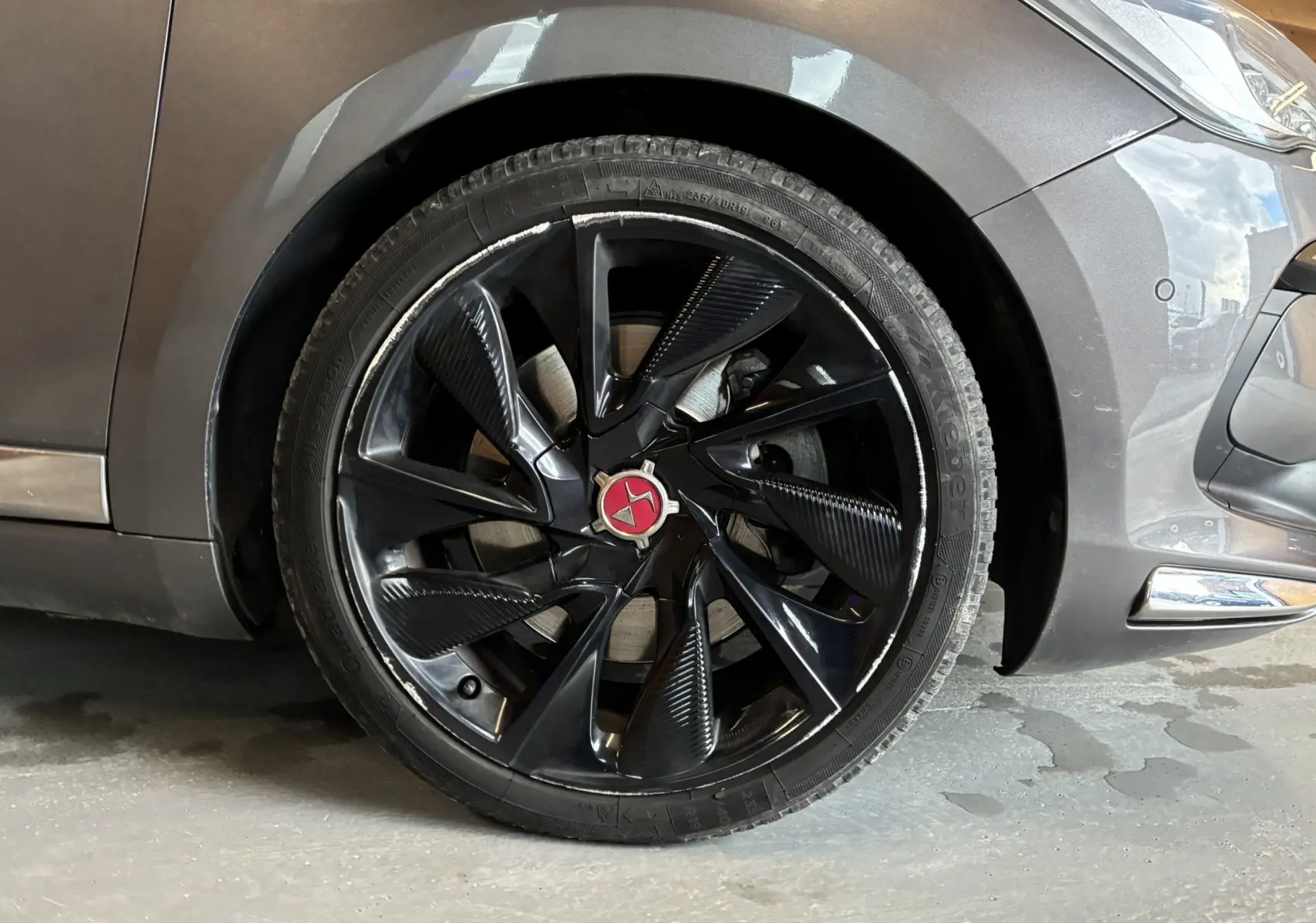 Gros plan sur la roue avant gauche d’une DS5 gris métallisé, mettant en valeur la jante noire au design moderne avec logo rouge central.