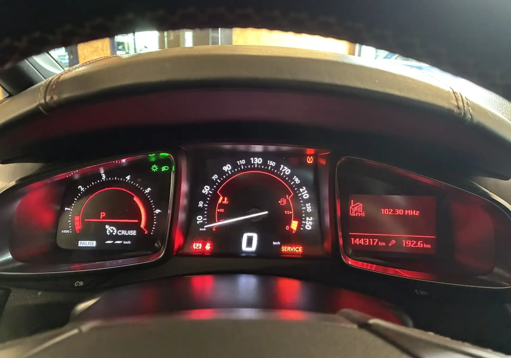 Vue rapprochée du tableau de bord numérique rougeoyant de la DS5 gris, affichant vitesse, compte-tours et radio FM.