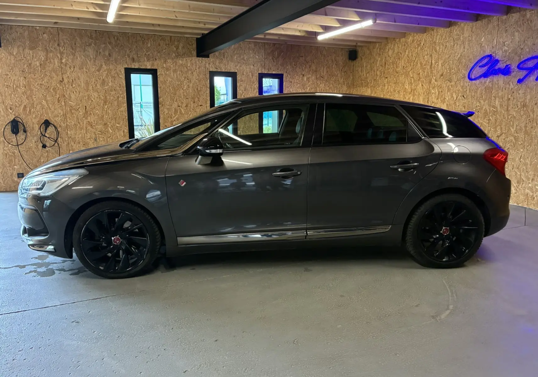 Vue de profil côté gauche d'une DS5 gris métallisé avec jantes noires, stationnée dans un garage au sol gris.