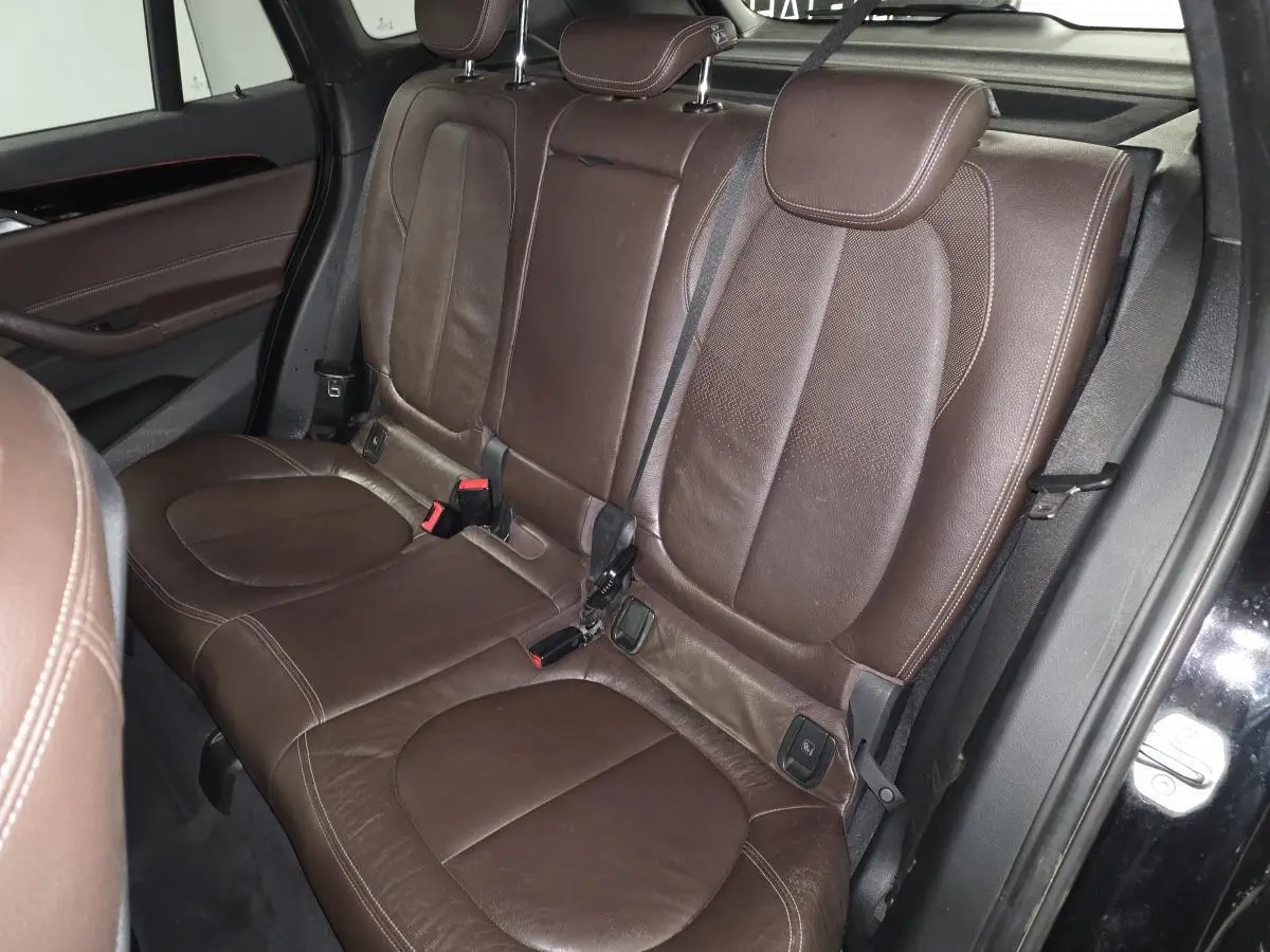 Vue intérieure sur la banquette arrière en cuir marron perforé du BMW X1 xDrive 25d noir, avec ceintures de sécurité visibles.