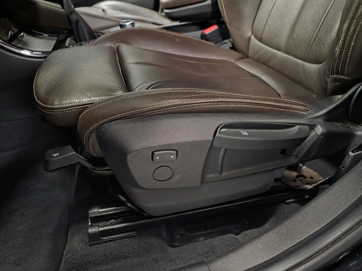 Gros plan sur le siège avant conducteur en cuir marron perforé avec commandes d'ajustement électrique sur BMW X1 noir.