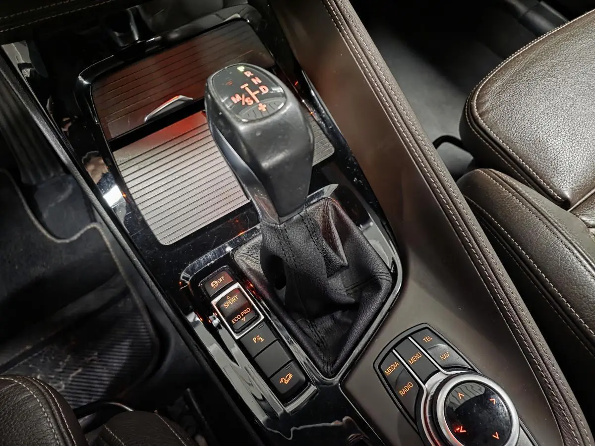 Gros plan sur la console centrale noire brillante avec levier de vitesses et commandes du BMW X1 xDrive 25d 2016 en cuir marron.