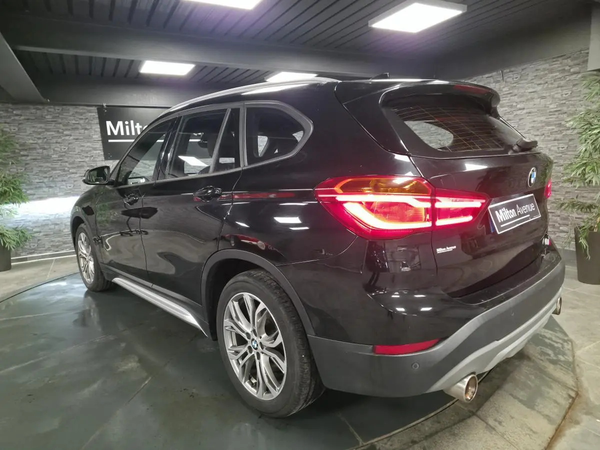 BMW X1 xDrive 25d noir vue 3/4 arrière droit, feux allumés et jantes alliage 18'' style 566 en Y.