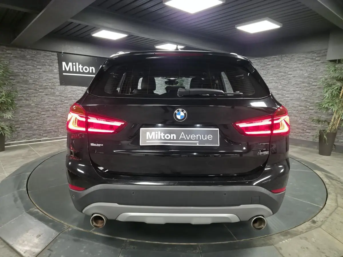 Vue arrière d'un BMW X1 xDrive 25d noir avec feux allumés et double sortie d'échappement chromée.