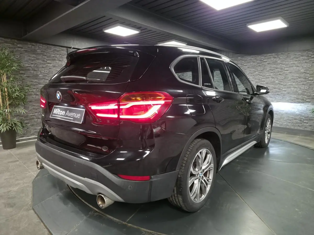 BMW X1 xDrive 25d noir vue 3/4 arrière droit, avec feux allumés et jantes alliage 18 pouces style 566 en Y.
