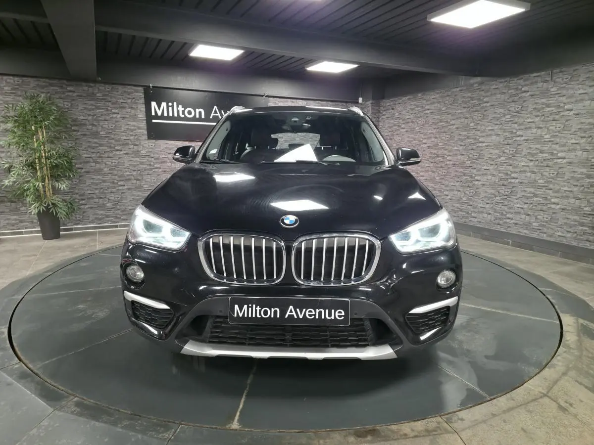 BMW X1 xDrive 25d noir vue de face avec calandre chromée et phares LED allumés en showroom.
