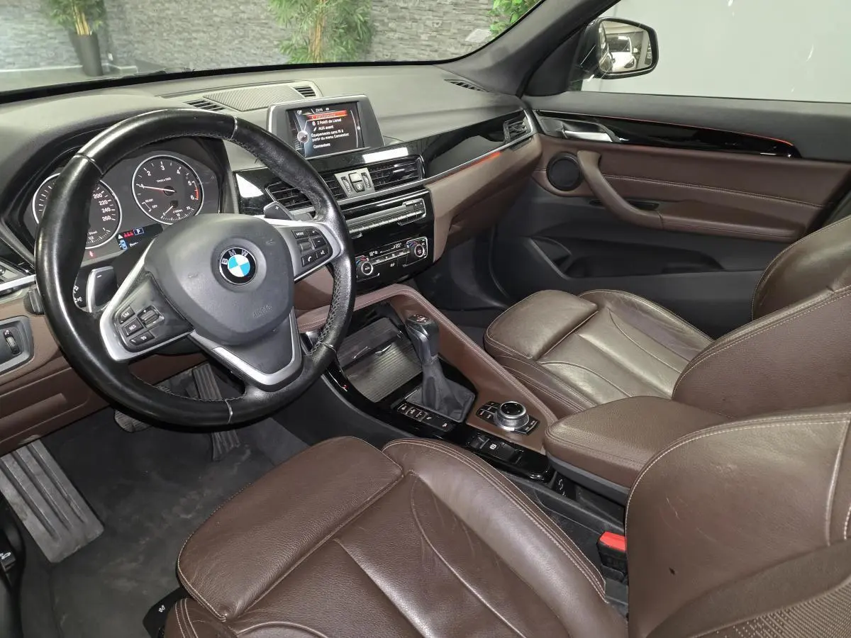 Vue intérieure côté conducteur du BMW X1 xDrive 25d 2016 avec sellerie cuir marron et tableau de bord noir brillant.