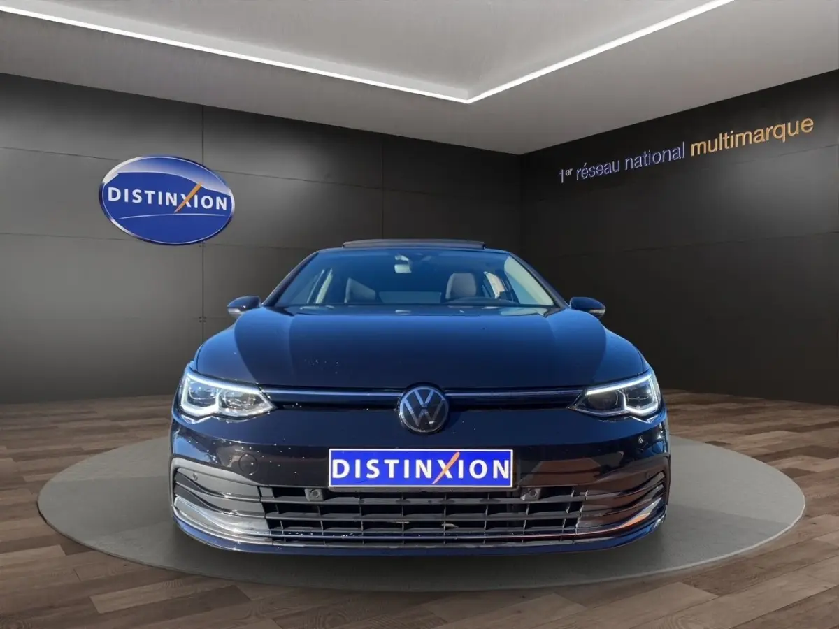 Volkswagen Golf noire vue de face avec toit panoramique et phares LED allumés en showroom.