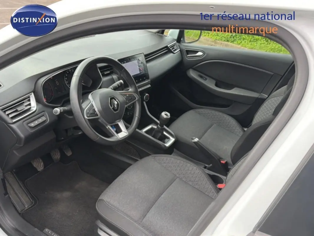 Vue intérieure côté conducteur de la Renault Clio blanche 2021, avec tableau de bord moderne et boîte manuelle.