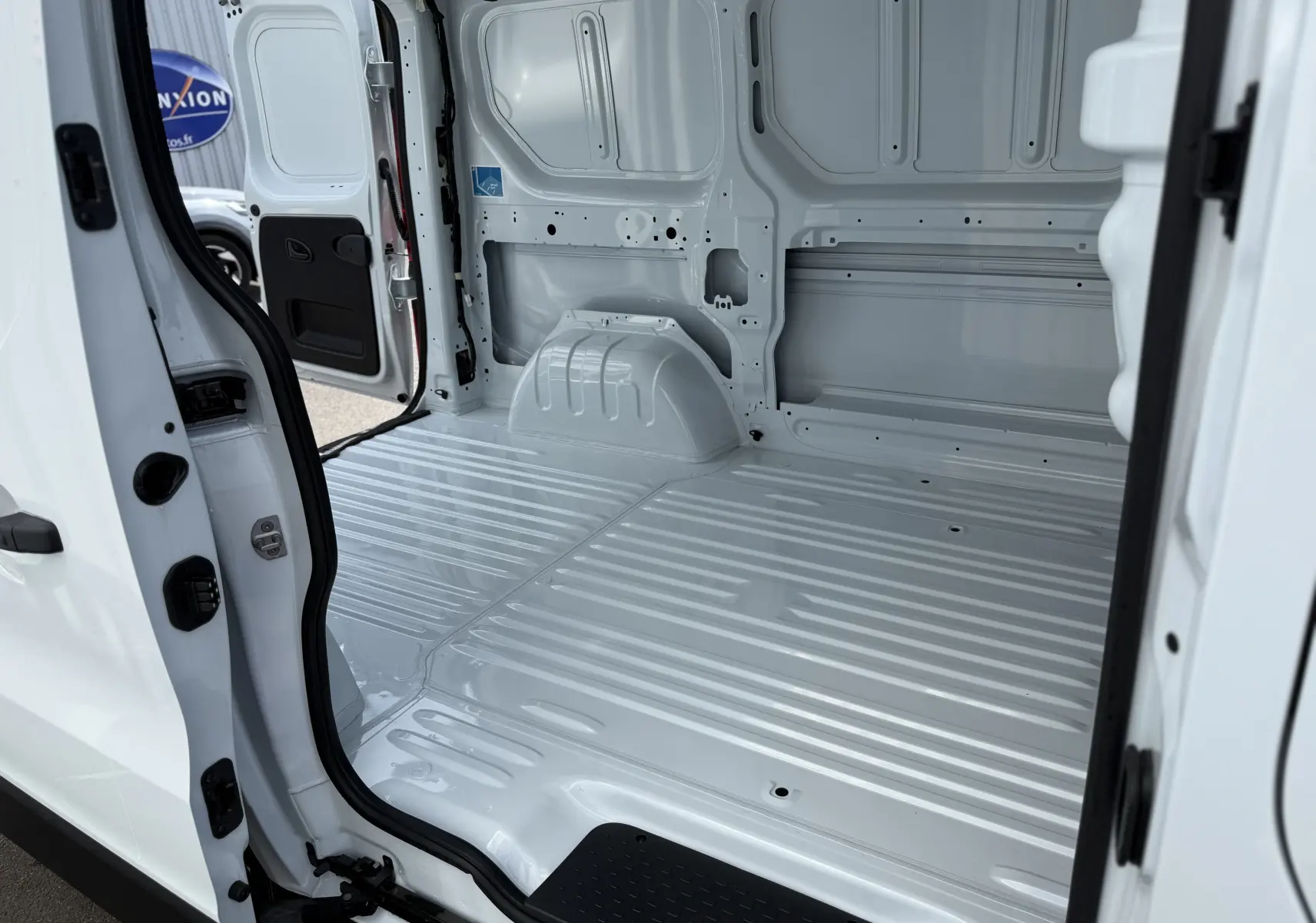 Intérieur du fourgon Renault Trafic blanc vu en ouverture latérale, montrant l’espace de chargement vide et métallique.