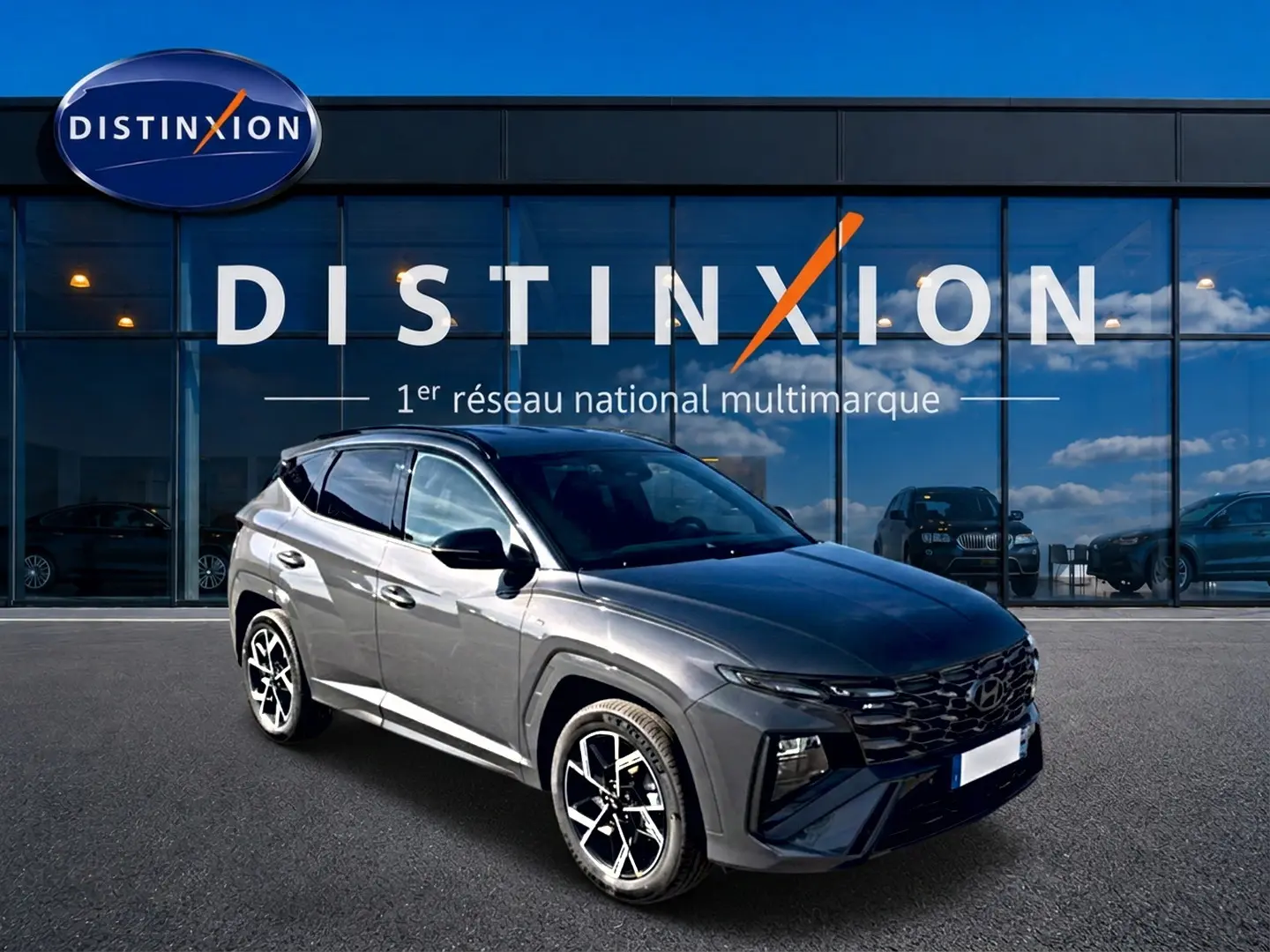 Hyundai Tucson 2026 gris écotronique en 3/4 avant droit avec calandre glossy black et jantes alliage 19 pouces.