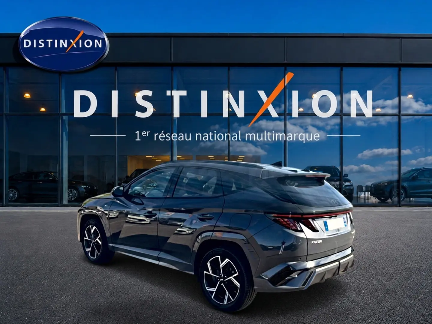 Vue 3/4 arrière droite du Hyundai Tucson 2026 gris ecotronique avec jantes alliage et feux arrière LED, devant une vitrine Distinxion.