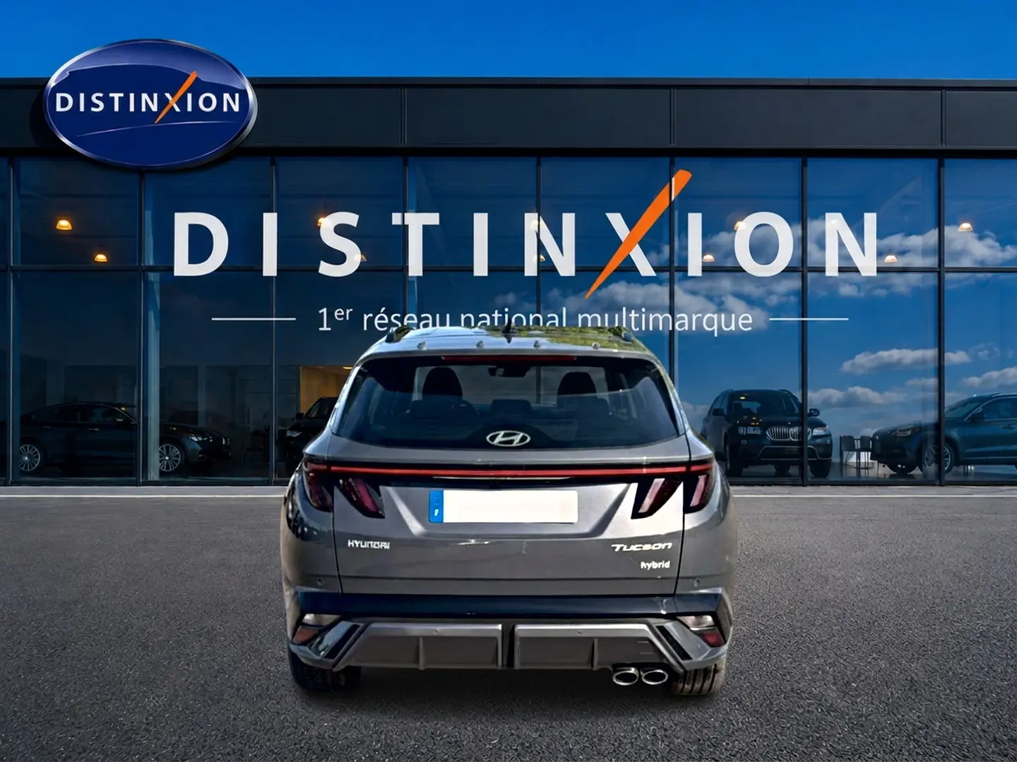 Vue arrière du Hyundai Tucson hybride gris ecotronique avec feux LED et double sortie d'échappement, devant une vitrine Distinxion.