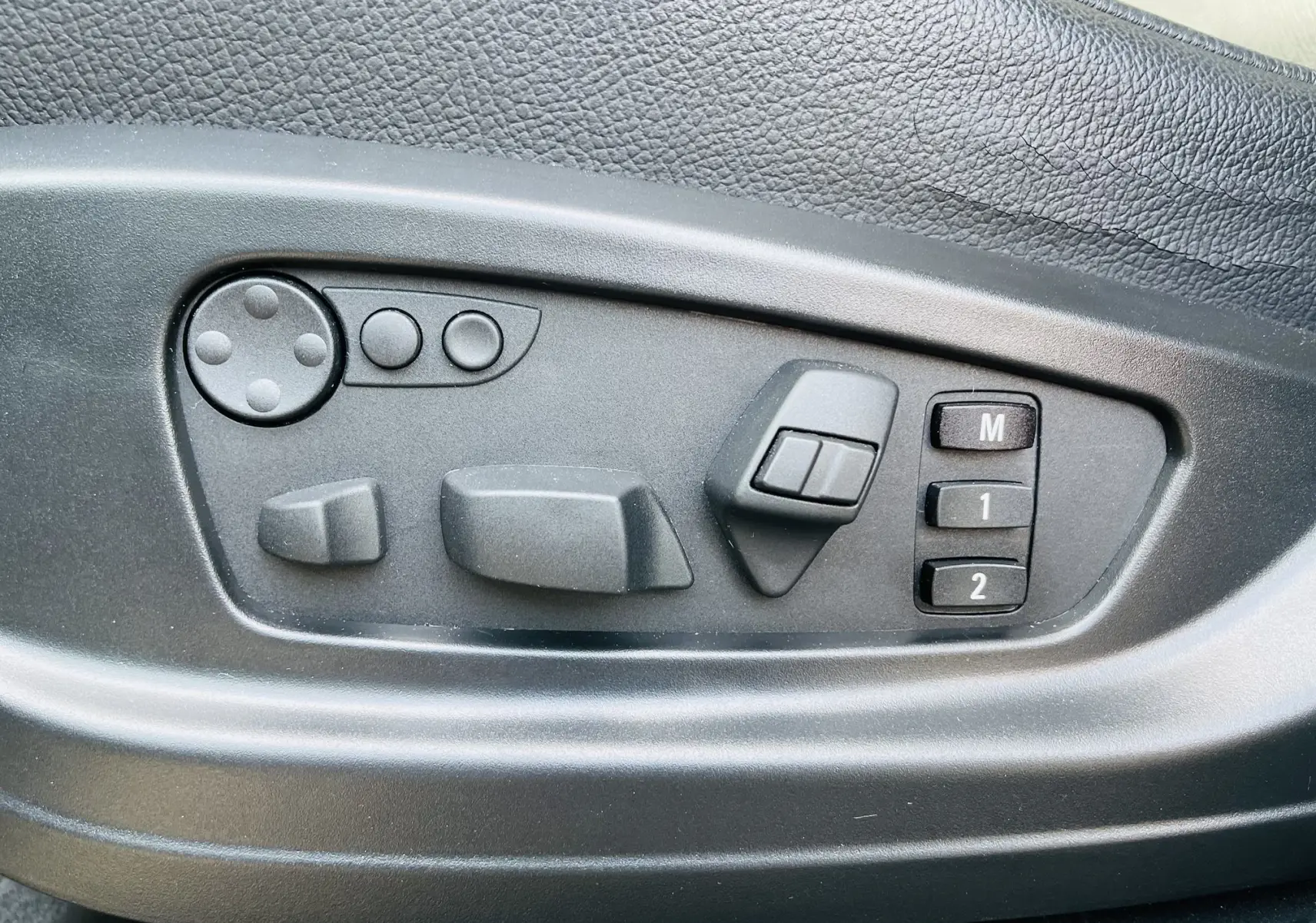 Panneau de réglage électrique des sièges côté gauche dans un BMW X6 blanc, avec mémorisation des positions.