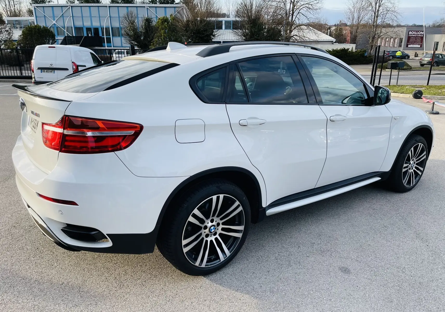 BMW X6 blanc en vue 3/4 arrière côté droit, avec jantes M sport et toit ouvrant visible.