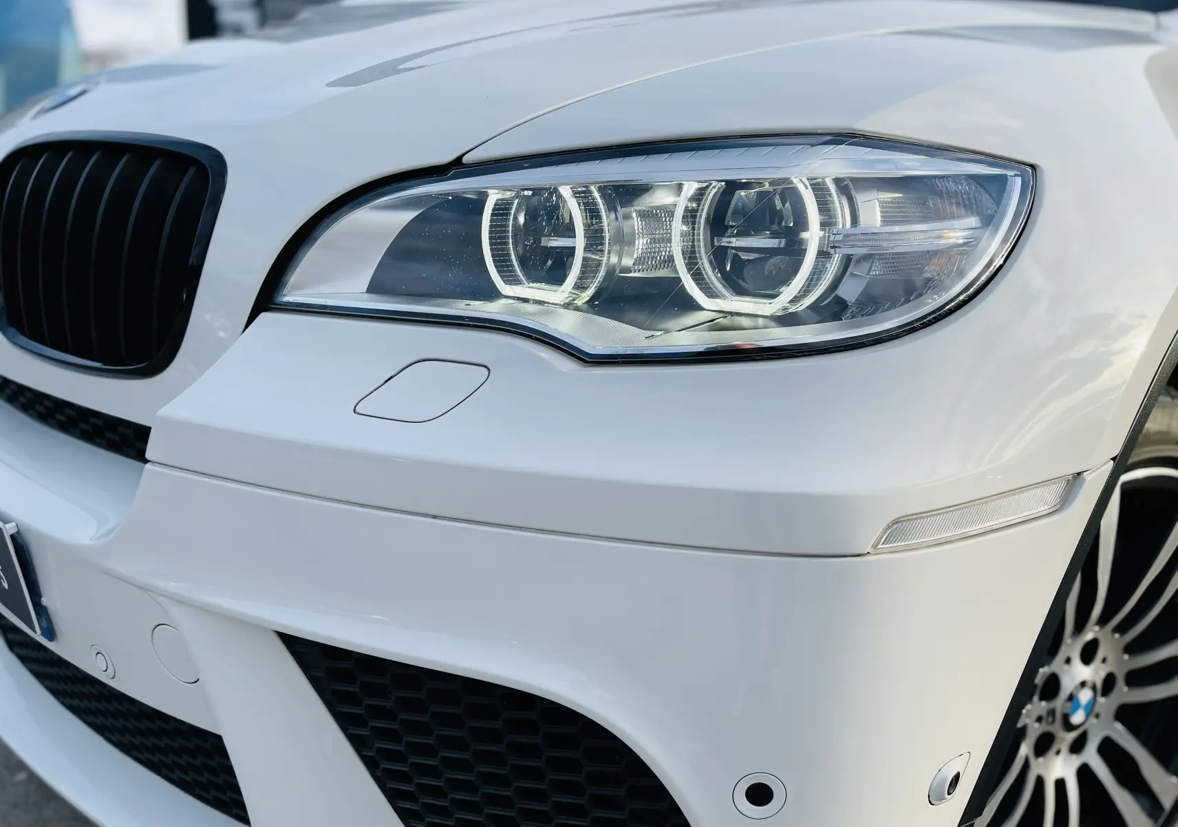 Gros plan sur l'avant droit blanc d'un BMW X6 50D M 2013, mettant en valeur le phare bi-xénon et la calandre noire.