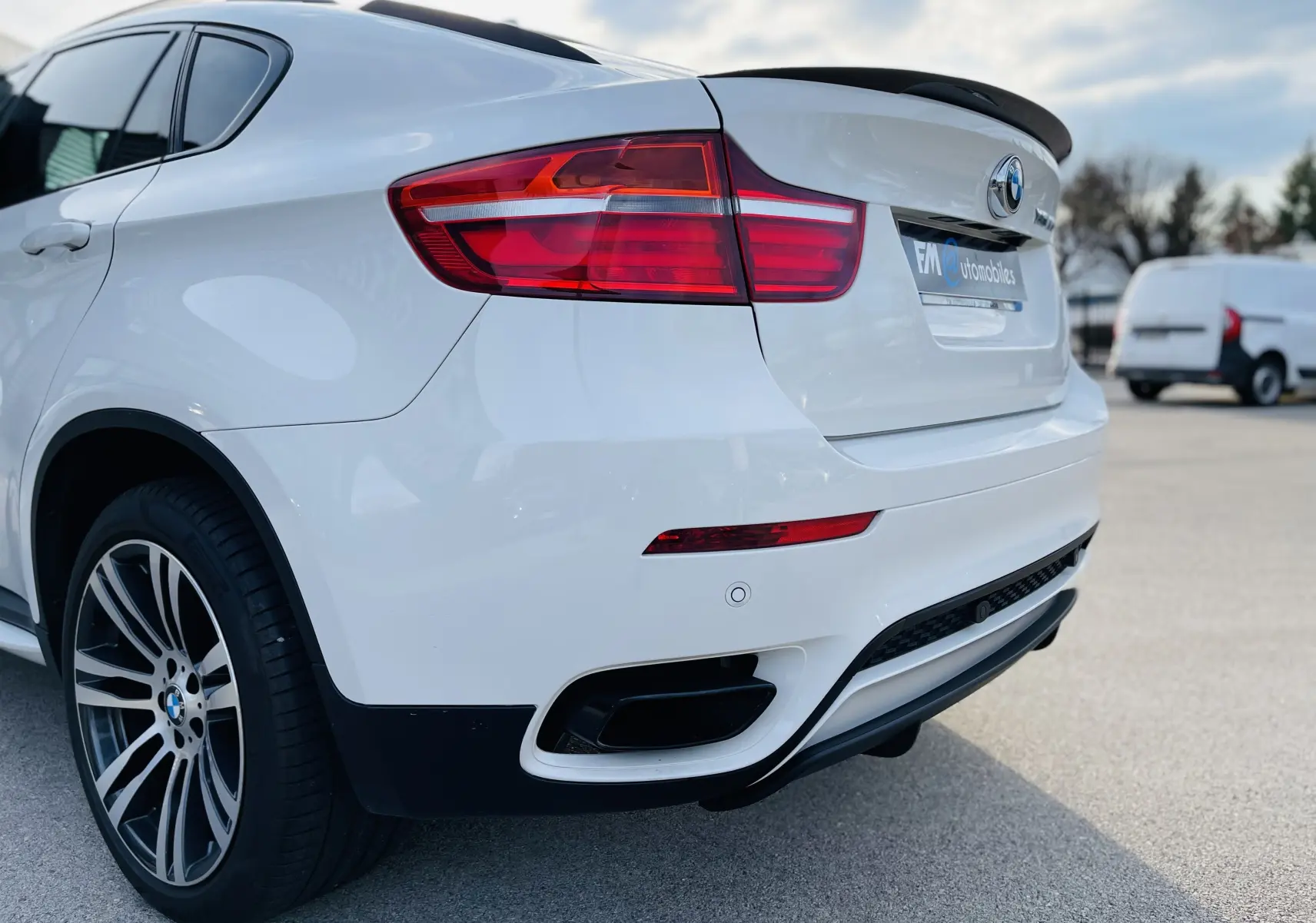 Vue 3/4 arrière droite d'un BMW X6 blanc avec feux arrière LED et double sortie d'échappement intégrée au pare-chocs.