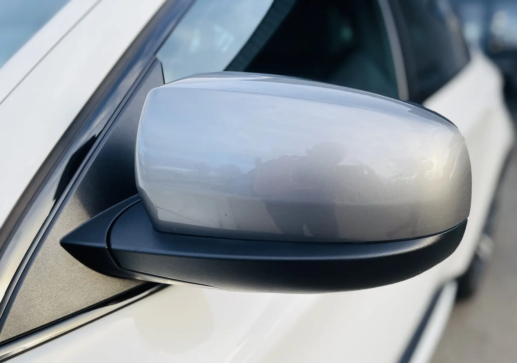 Gros plan sur le rétroviseur droit gris argenté du BMW X6 blanc, mettant en valeur sa finition lisse et brillante.