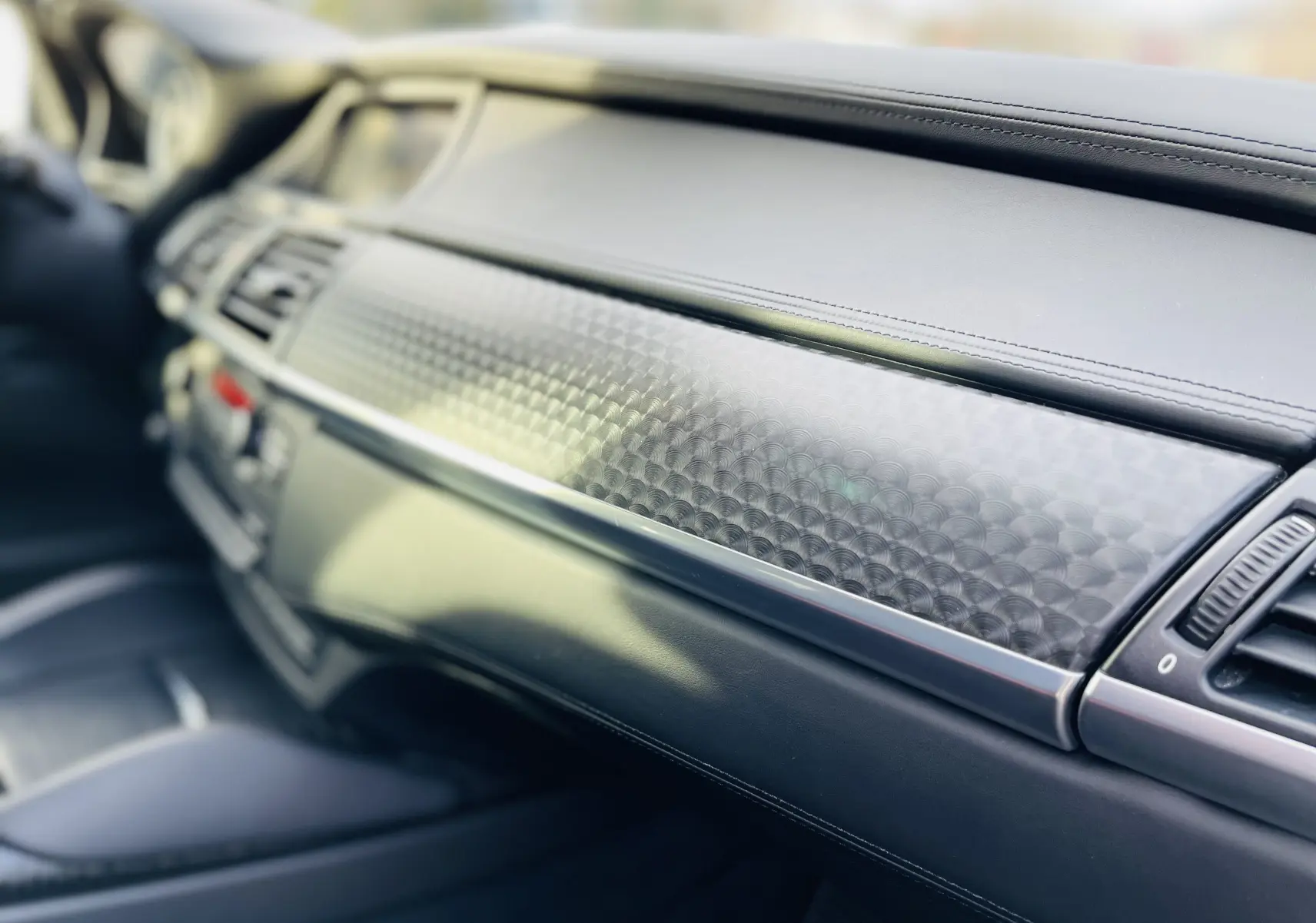 Détail du tableau de bord noir avec insert décoratif texturé du BMW X6 50D M blanc, vue intérieure côté passager.