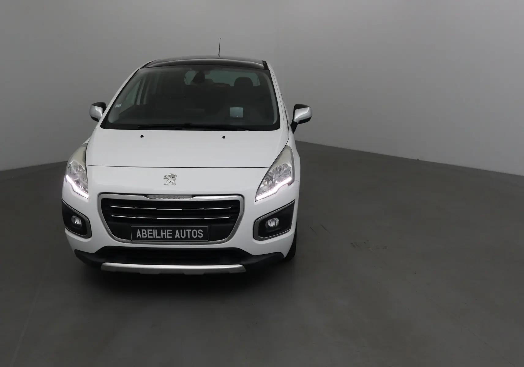 Peugeot 3008 blanc vue de face avec phares allumés dans un studio neutre.