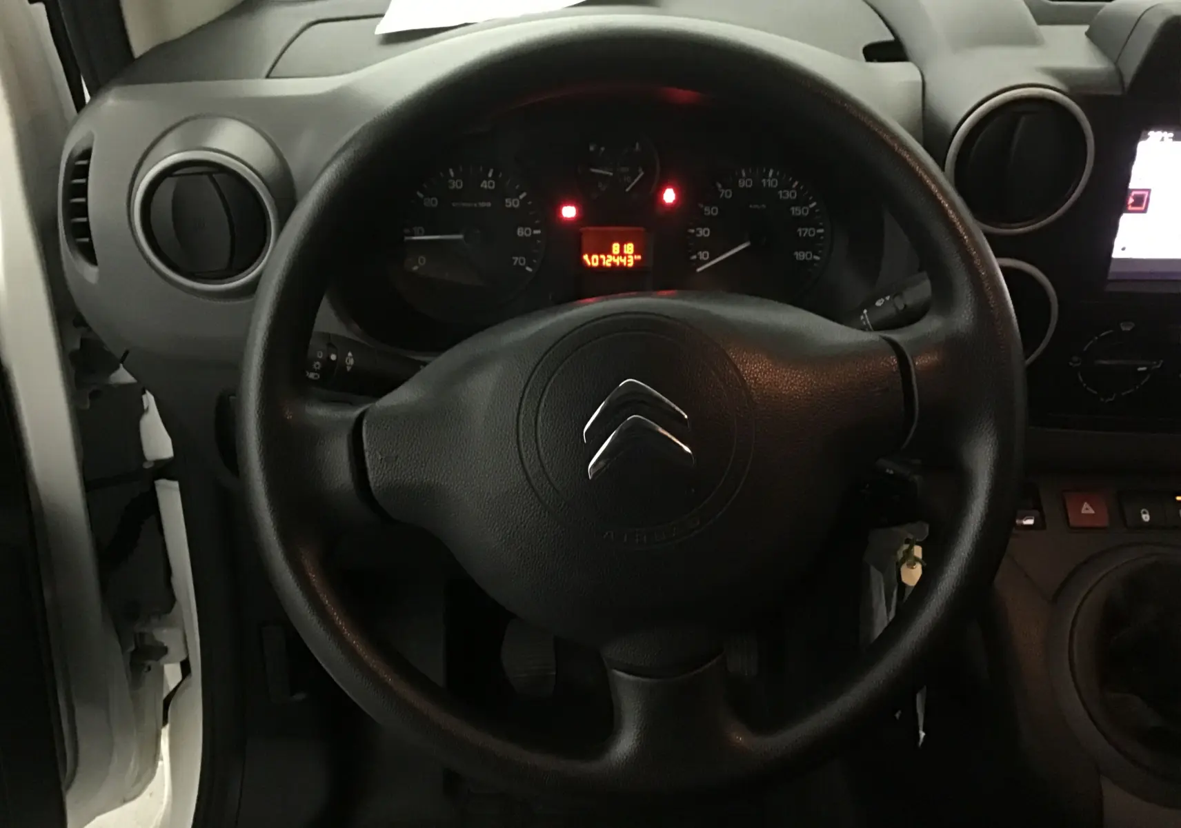 Vue intérieure centrée sur le volant noir d'un Citroën Berlingo blanc 2018 avec tableau de bord et compteur allumé.