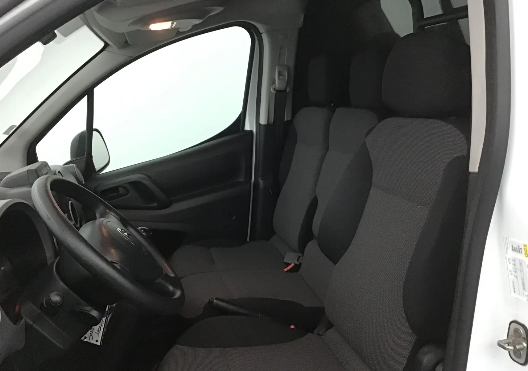 Vue intérieure côté conducteur du Citroën Berlingo blanc 2018, montrant les sièges avant et le volant noir.