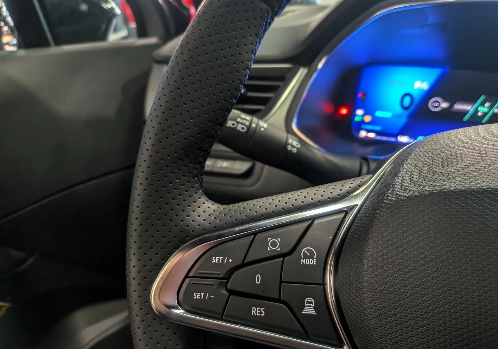 Gros plan sur les commandes au volant en cuir perforé du Renault Symbioz gris Cassiopé, tableau de bord numérique en arrière-plan.