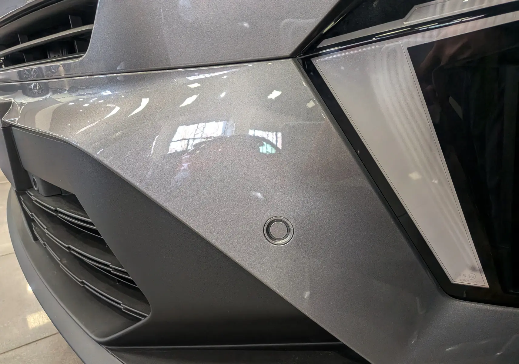 Gros plan sur le pare-chocs avant gris Cassiopé du Renault Symbioz E-Tech, mettant en valeur le capteur de stationnement rond.