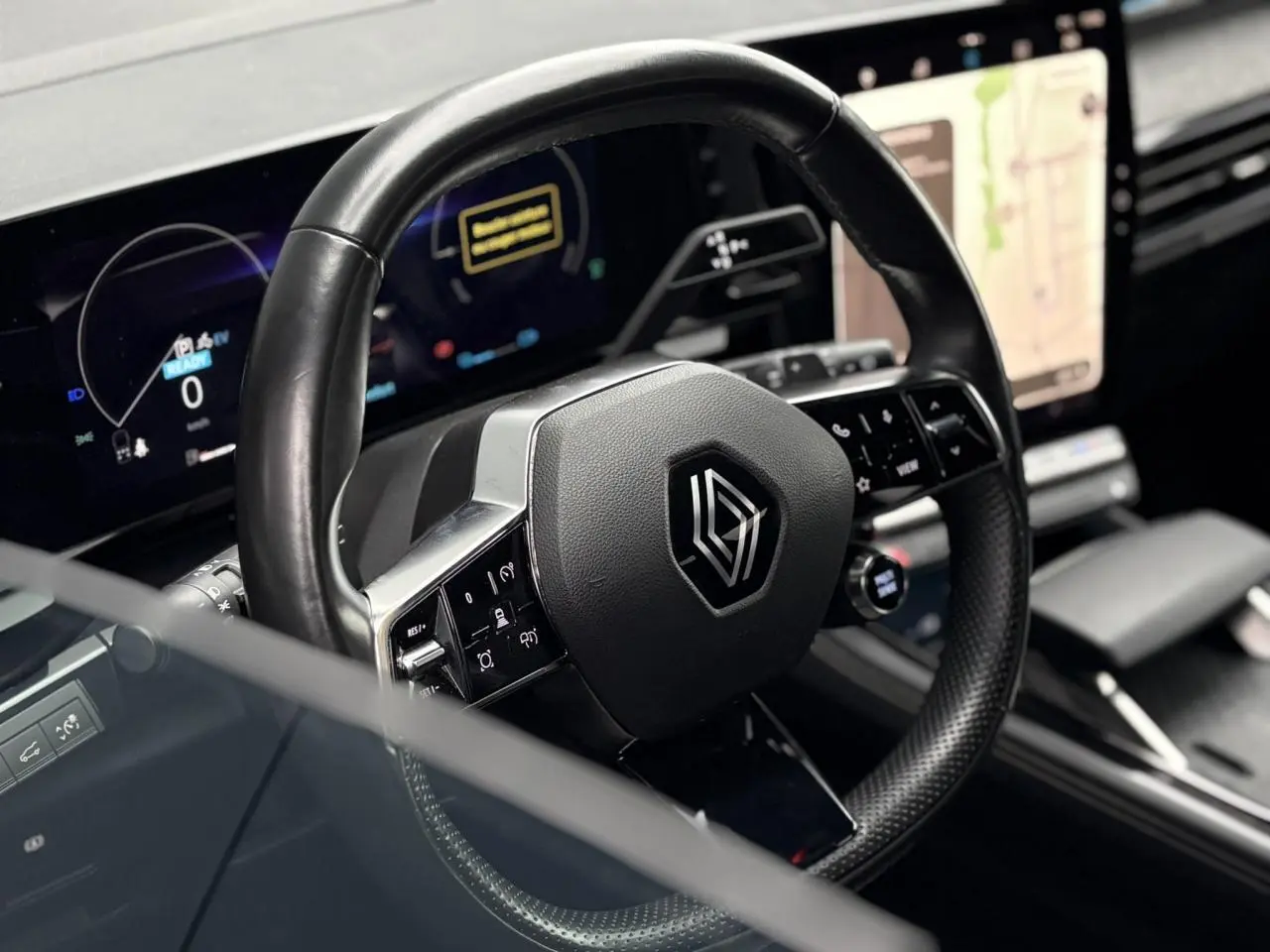 Vue rapprochée du volant noir de la Renault Espace 2024 avec commandes intégrées et écran tactile en arrière-plan.