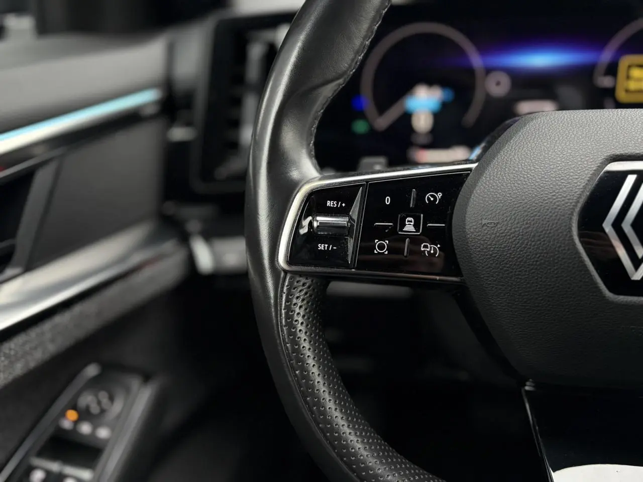 Gros plan sur le volant noir perforé avec commandes intégrées du Renault Espace 2024, intérieur sombre.