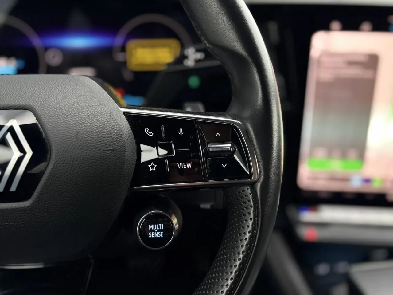 Gros plan sur le volant noir perforé du Renault Espace 2024 avec commandes multifonctions et bouton Multi-Sense éclairé.