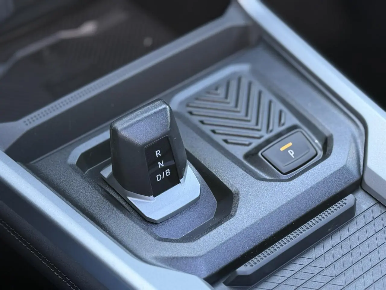 Gros plan sur la commande de boîte automatique et bouton de frein de parking du Dacia Bigster 1.8 Hybrid bleu Indigo.