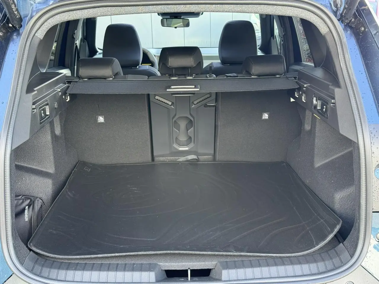Coffre ouvert vu de l'arrière du Dacia Bigster bleu indigo, avec tapis de protection et banquette arrière visible.