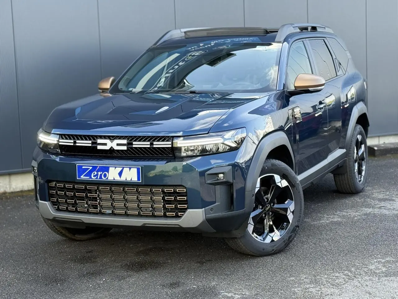 Vue 3/4 avant droit du Dacia Bigster 1.8 Hybrid bleu indigo avec jantes alliage noires et rétroviseurs dorés.