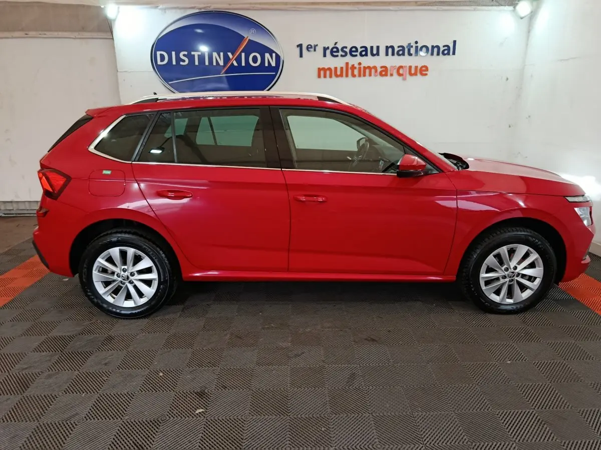 Vue de profil côté droit d'un Skoda Kamiq rouge 2024 avec rails de toit noirs dans un showroom.