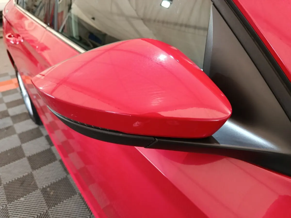 Gros plan sur le rétroviseur côté gauche rouge vif du Skoda Kamiq 2024 avec carrosserie et vitre partiellement visibles.