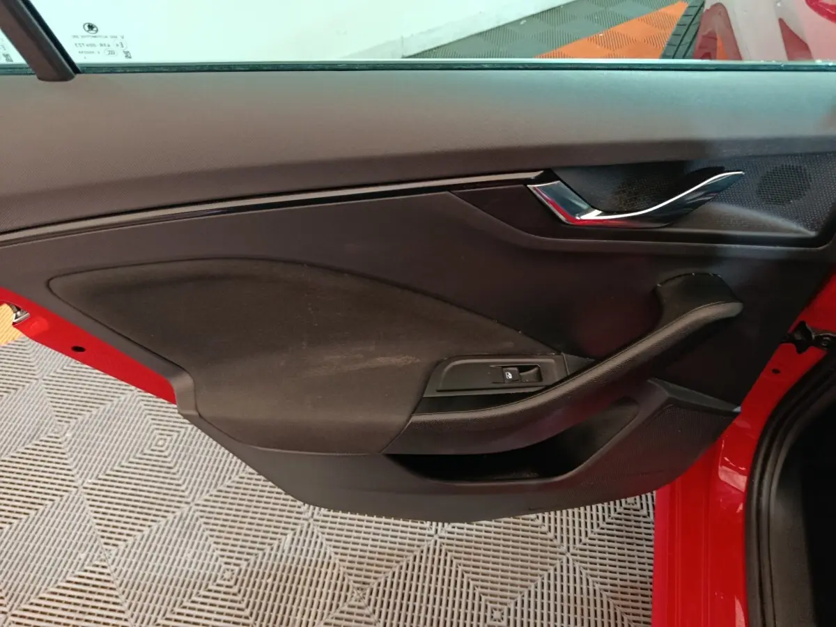 Vue intérieure de la porte avant gauche rouge d'une Skoda Kamiq 2024 avec poignée chromée et commande de vitre électrique.