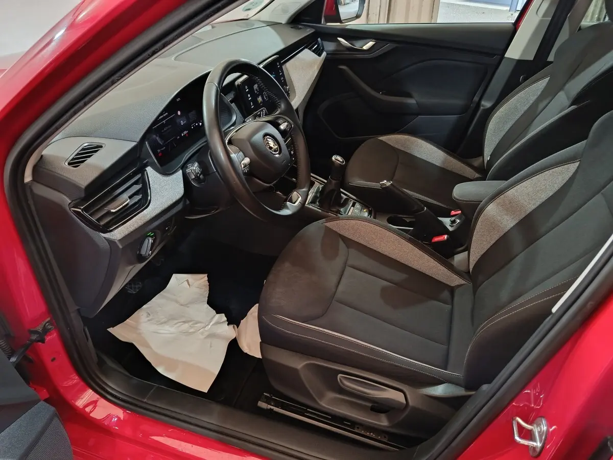 Vue intérieure côté conducteur du Skoda Kamiq rouge 2024, volant cuir multifonctions et sièges tissu bicolores.
