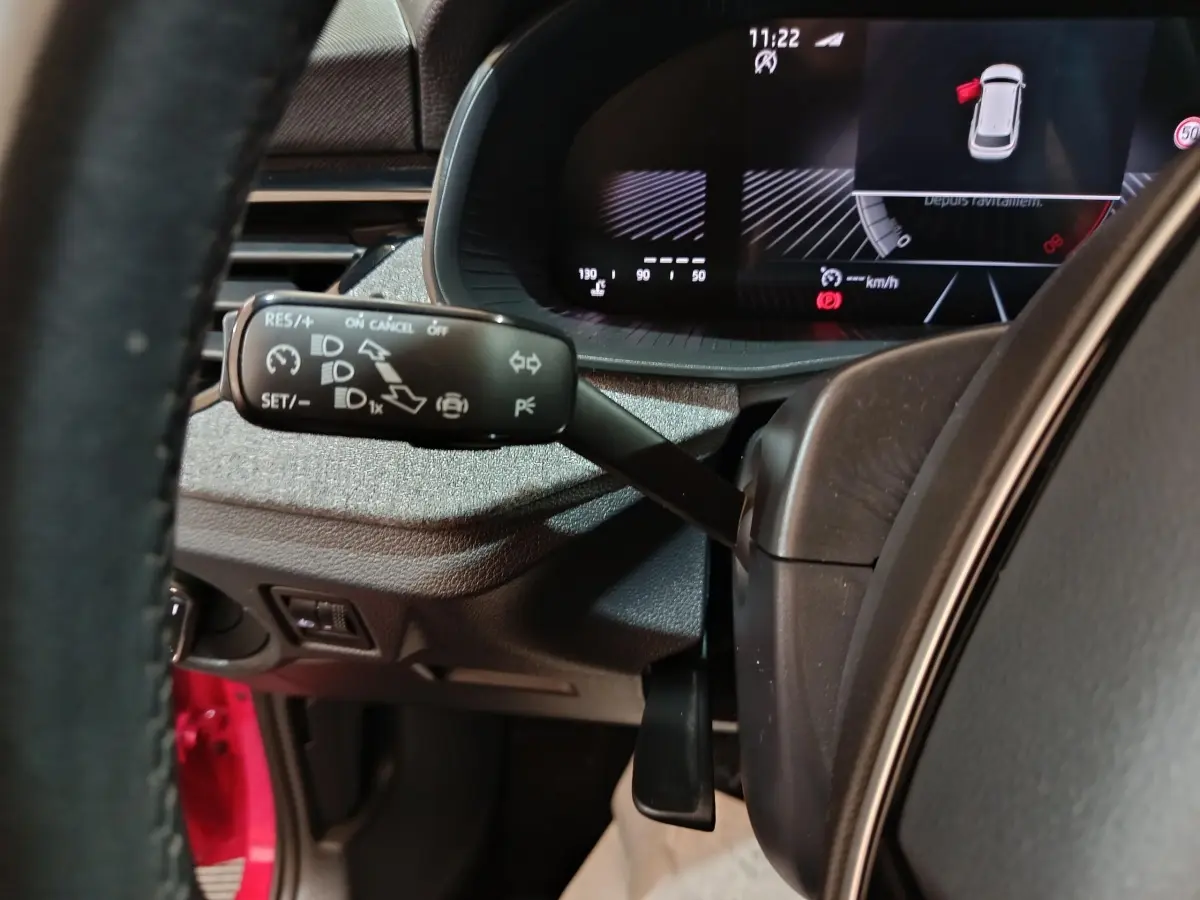 Gros plan sur le commodo gauche du volant cuir d’un Skoda Kamiq rouge, avec tableau de bord numérique en arrière-plan.