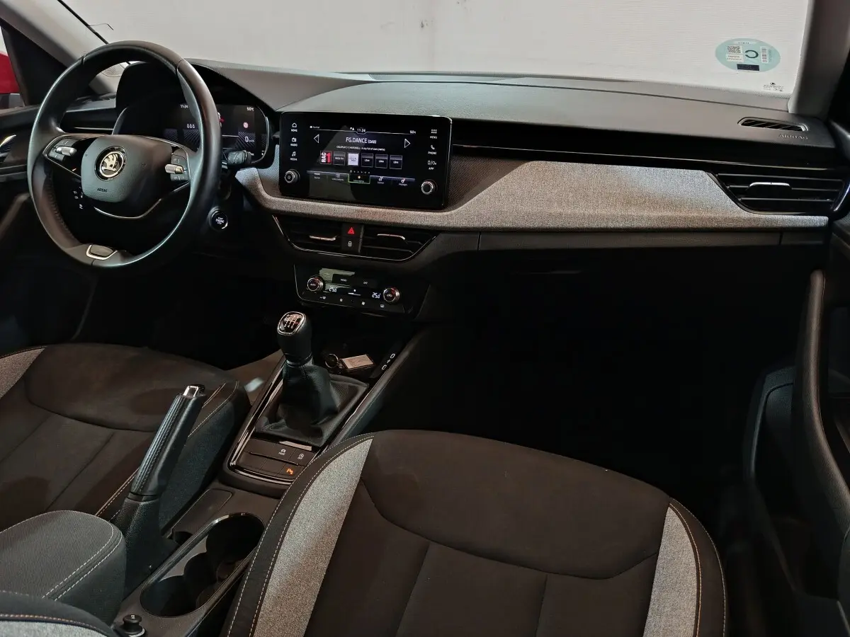 Vue intérieure avant du Skoda Kamiq 2024, volant cuir noir, tableau de bord avec écran tactile central et levier de vitesses manuel.