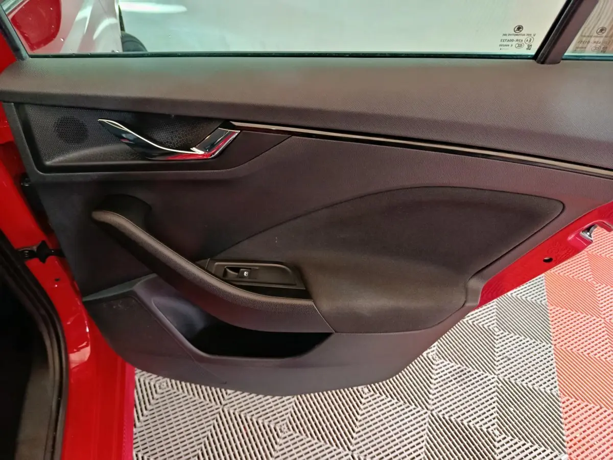Vue intérieure côté gauche de la porte avant rouge du Skoda Kamiq 2024 avec poignée chromée et commande de vitre électrique.
