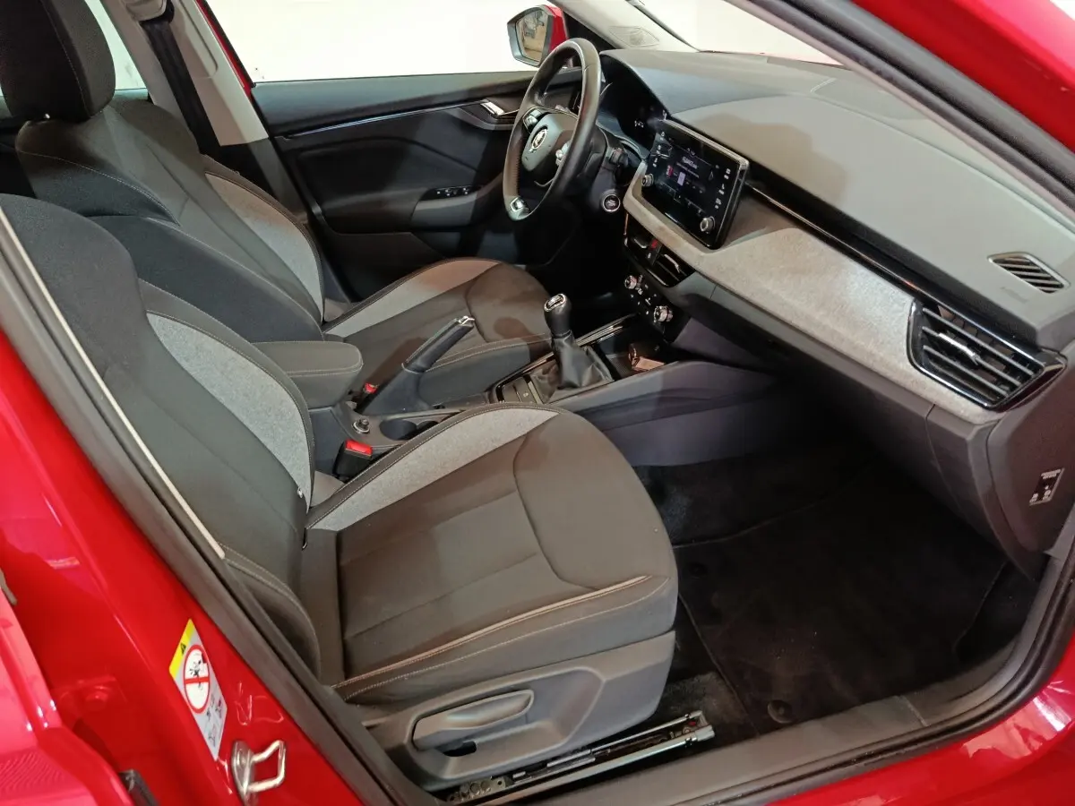 Intérieur côté conducteur d’une Skoda Kamiq rouge 2024, montrant sièges tissu bicolore et tableau de bord avec écran tactile.
