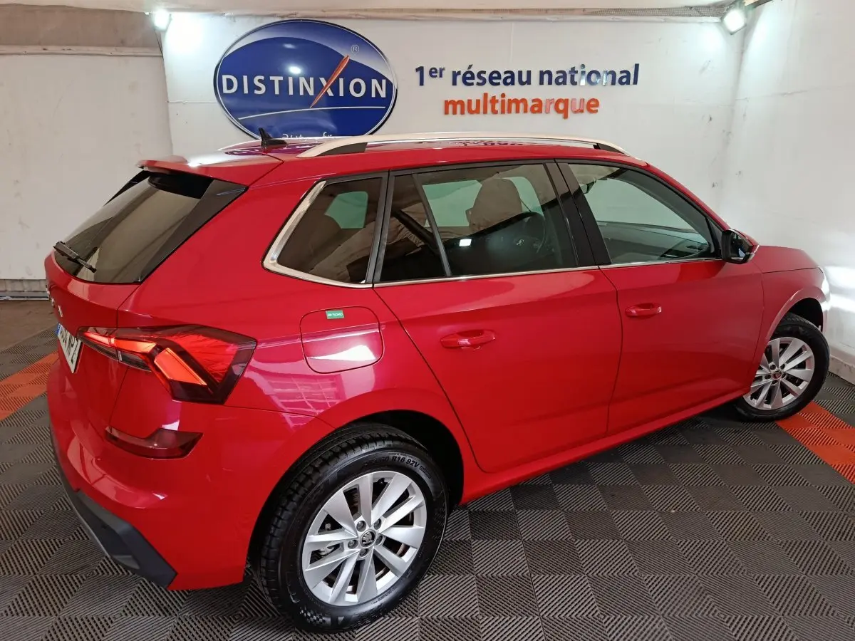 Vue 3/4 arrière droite d’un Skoda Kamiq rouge 2024 avec barres de toit noires et vitres teintées.