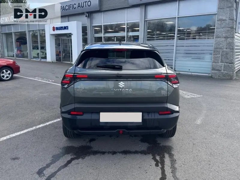 Vue arrière d'un Suzuki Vitara électrique 2026 en vert Land Breeze avec toit noir, garé devant un concessionnaire.