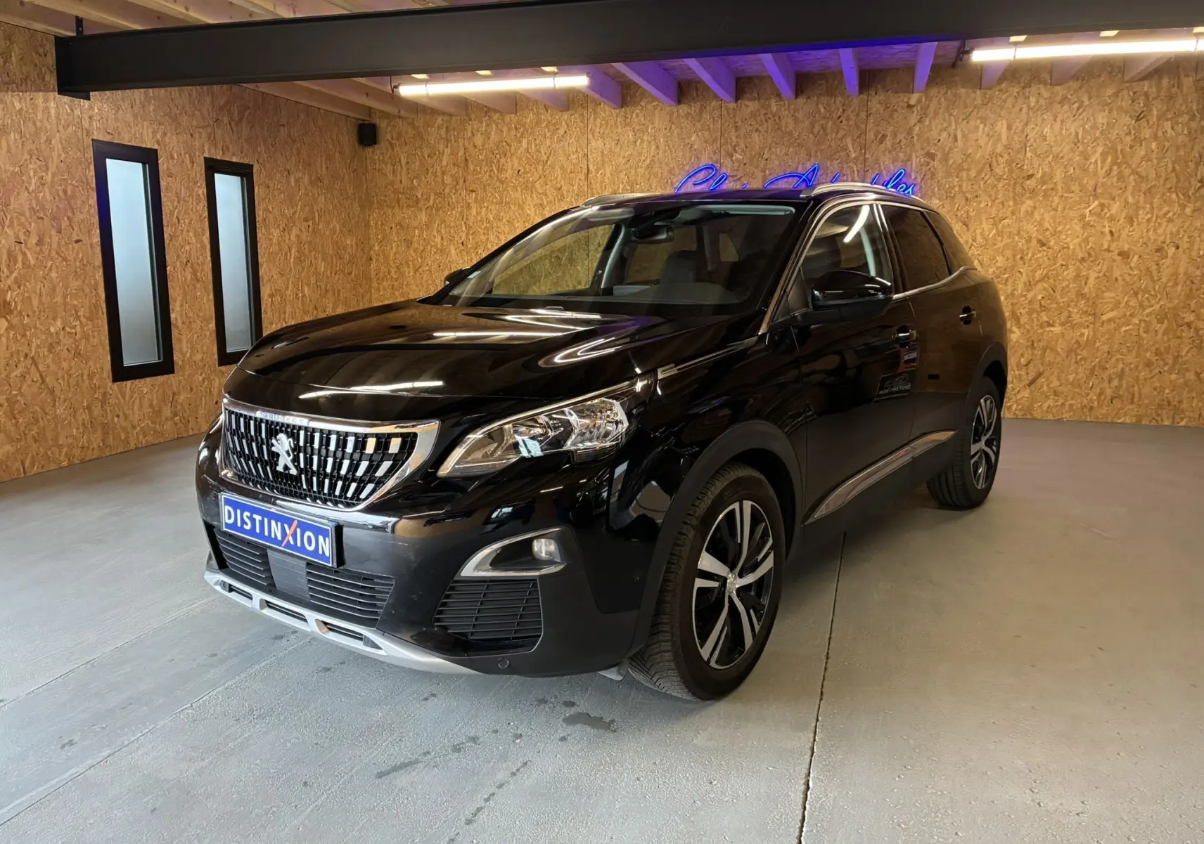 Peugeot 3008 noir vue 3/4 avant droit dans un intérieur avec murs en bois et éclairage fluorescent.