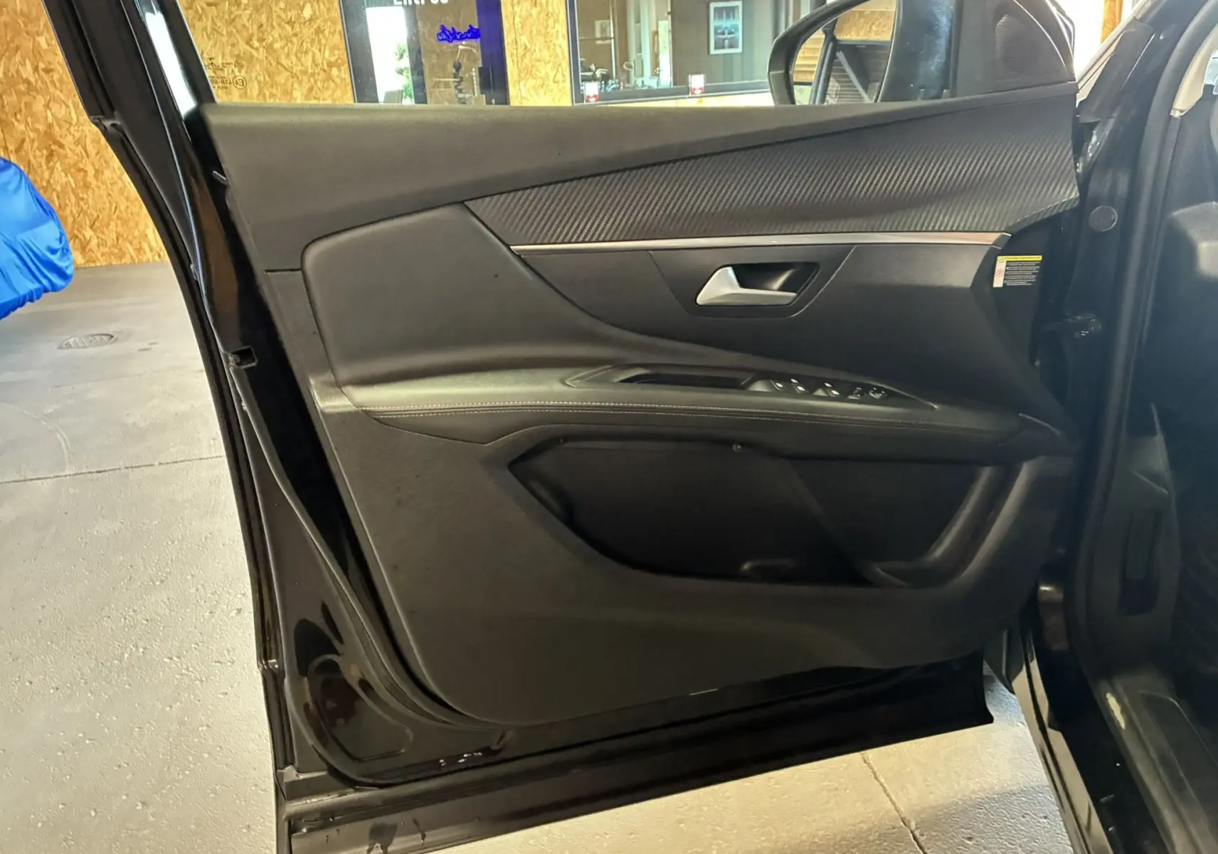 Vue intérieure côté gauche de la porte avant noire du Peugeot 3008 1.5 BlueHDi 130 Allure Pack avec commandes de vitres.